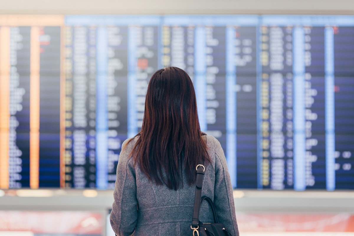 Lady with long dark hair standing in front of departure board 